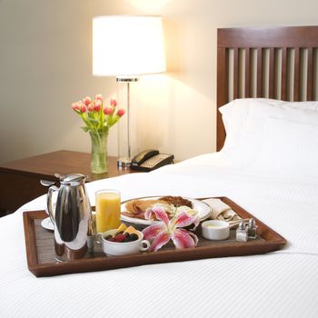 Breakfast tray laying on white bed in upscale hotel.