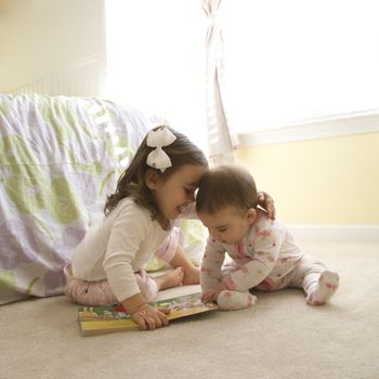 Caucasian girl children sitting on bedroom floor looking at book.