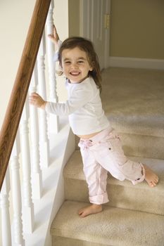 Caucasian girl toddler standing on carpeted stairs holding onto railing.