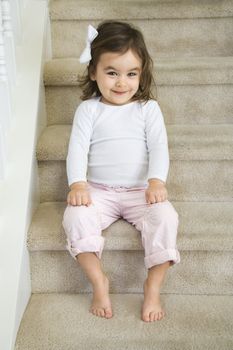 Caucasian girl toddler sitting on carpeted stairs.