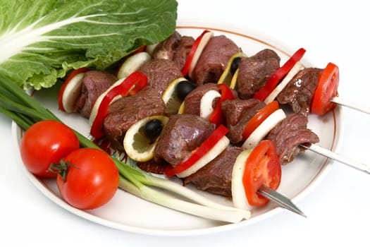 Appetizing shish kebab with tomatoes, an onions, greens, olives and a lemon