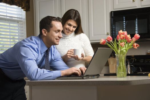 Caucasian couple in kitchen with coffee looking at laptop computer.