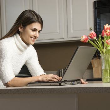 Caucasian woman in kitchen looking at laptop computer.