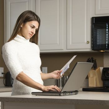 Caucasian woman in kitchen looking at laptop computer.