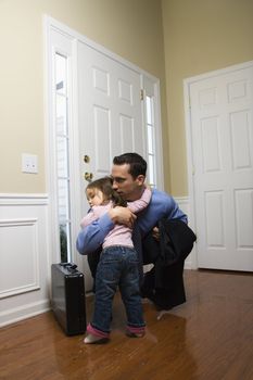 Caucasian businessman at door with briefcase hugging daughter.