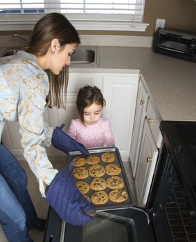 Caucasian mother and daughter taking cookies out of oven.