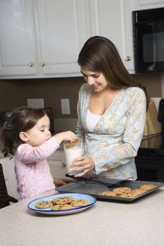 Caucasian mother holding milk glass while daughter dunks cookie.