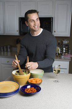 Caucasian man making salad on kitchen counter.