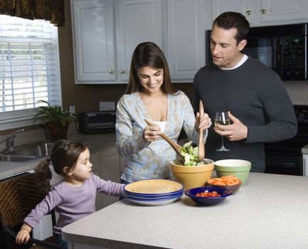 Caucasian woman making salad on kitchen counter with daughter and husband.