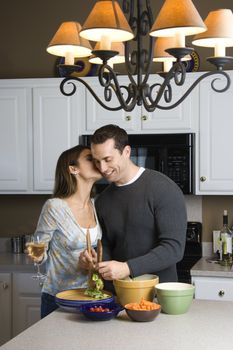 Caucasian woman kissing man at kitchen counter.