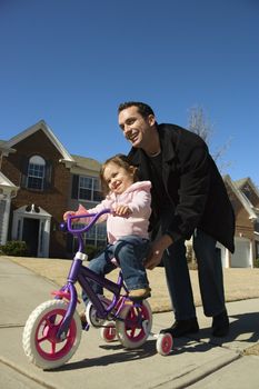 Caucasian father helping daughter ride bicycle.