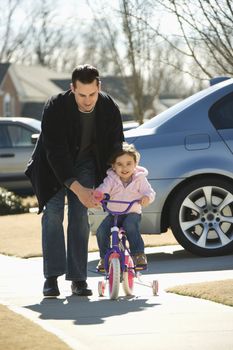 Caucasian father helping daughter ride bicycle.