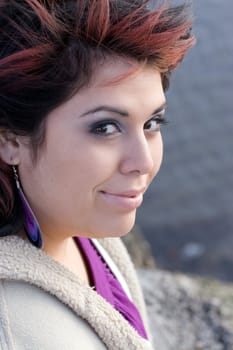 Portrait of a young Spanish woman with red highlights in her hair by the ocean.