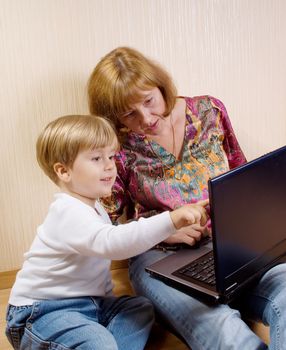 Mother and her son siting on a floor looking the laptop