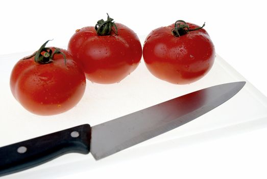 White plastic cutting board with a knife and tomato isolated on a white background.