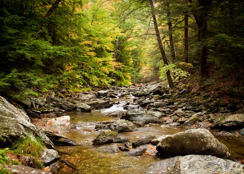 Long duration image of water flowing over boulders and mossy rocks in autumn