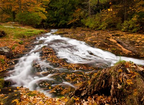 Long duration image of water flowing over boulders and mossy rocks in autumn