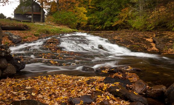 Long duration image of water flowing over boulders and mossy rocks in autumn
