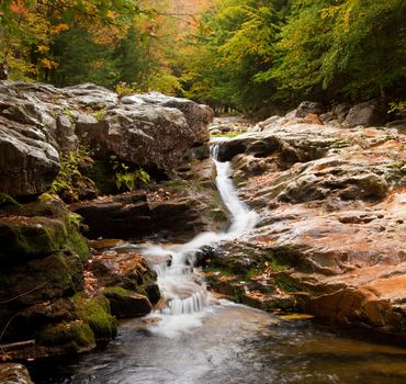 Long duration image of water flowing over boulders and mossy rocks in autumn