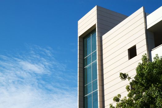 Corner of a building and elevator tower enclosed by green glass with blue sky and tree background