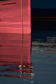 reflections in the water in front of a pink boat in the port of Socoa