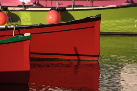 three small  boats moored in the port of Socoa, two red and one green.