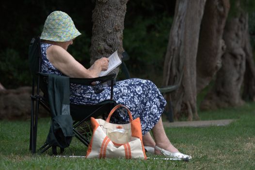 an old lady reading a book sitting on a chair, hat on head, in a garden of St Jean de Luz in the Basque country, France