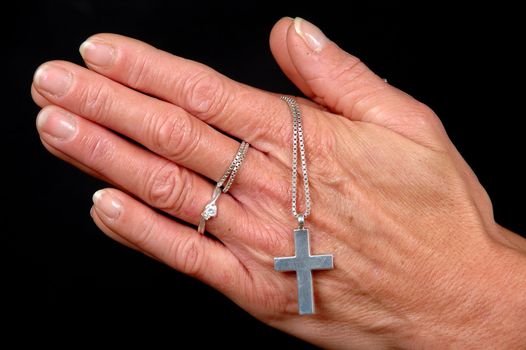 Woman is praying holding her cross. On black clean background.