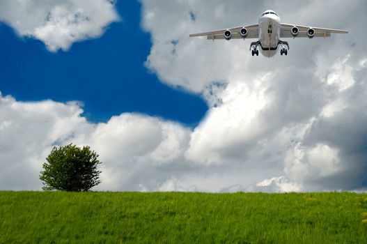 Plane is flying over a very beautiful hill with a green tree. The main focus is on the plane.