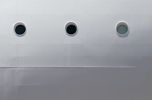 a row of three portholes on the site of a cruise ship