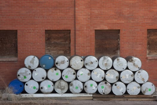 stack of empty oil drums against brick wall with boarded windows of abandoned factory