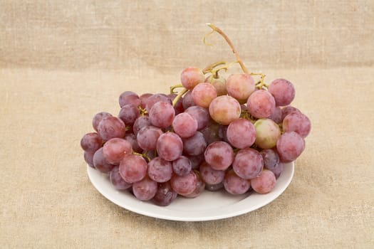 Ripe red grape on plate on textile background