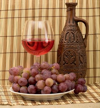 Stil life with carafe, grape and goblet on mat