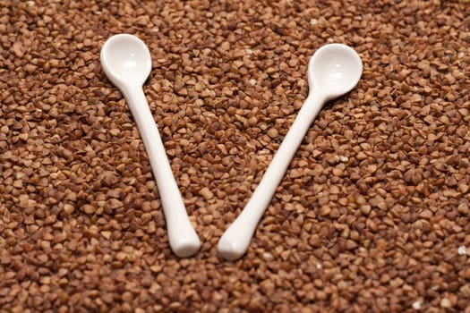 Two ceramic spoons on background from buckwheat