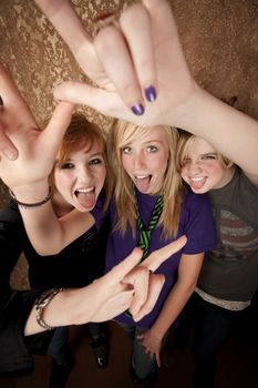 Portrait of three pretty young girls on a gold background making bull horn gestures