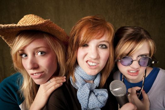 Portrait of three pretty young girls with a microphone making faces on green background