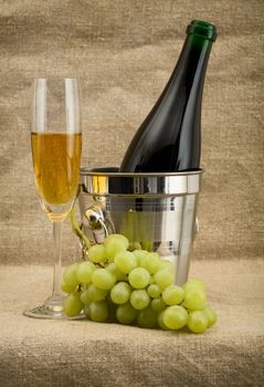 Still life with champagne bottle, bucket, goblet and grapes