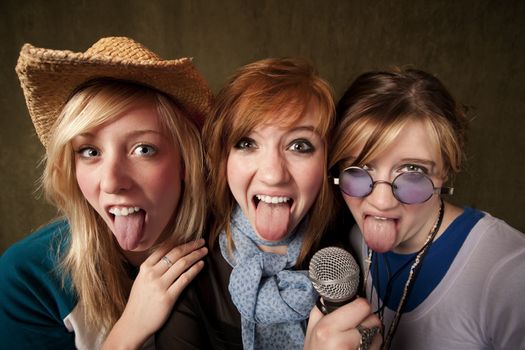 Portrait of three pretty young girls and tongues out with a microphone on green background