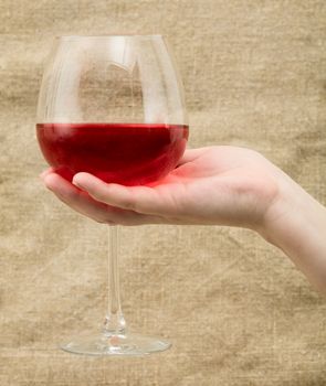 Wineglass with wine on female hand on canvas background