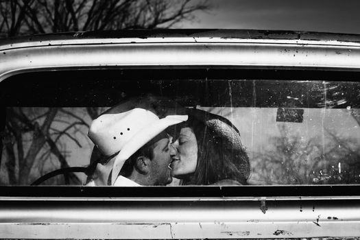 Cowboy and girlfriend kissing in through the back window of a pickup truck