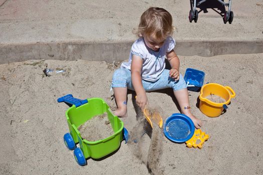 Cute Caucasian baby girl playing with the sand in sandpit.