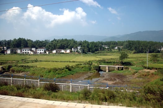 Chinese village in Hunan province. General landscape with river, rice fields, hills and trees.