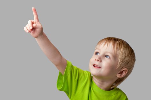The boy points his finger upward. Half-length portrait, arms down. Gray  background
