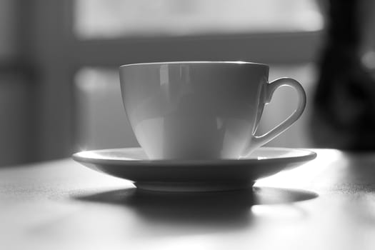 White ceramic mug with a saucer on a soft gray background. Concept bar, cafe or restaurant. Black and white photography.