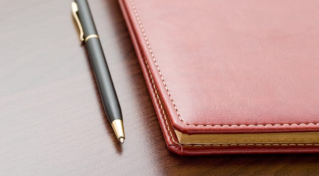 Leather notebook and a black pen on a dark desktop.