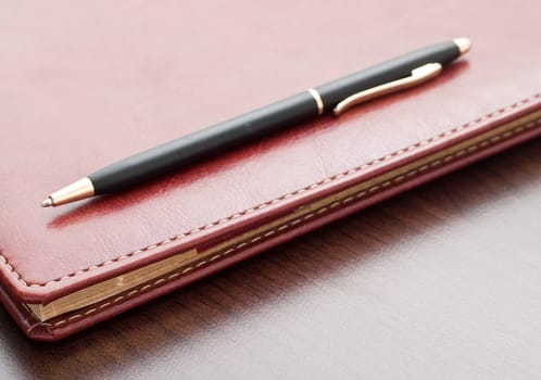 Leather notebook and a black pen on a dark desktop.