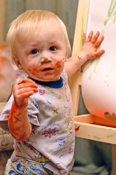 The boy was all covered with paint against the backdrop of his drawings. 