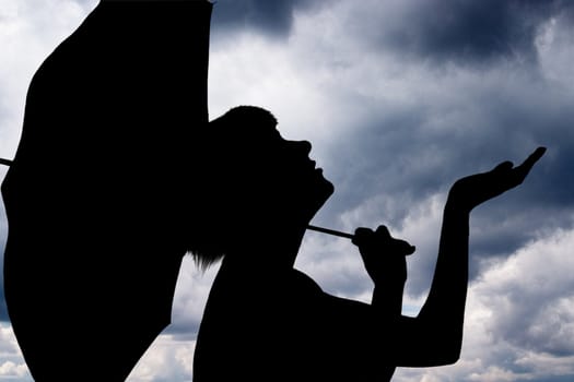 Silhouette of the young girl with an umbrella againist cloudy background