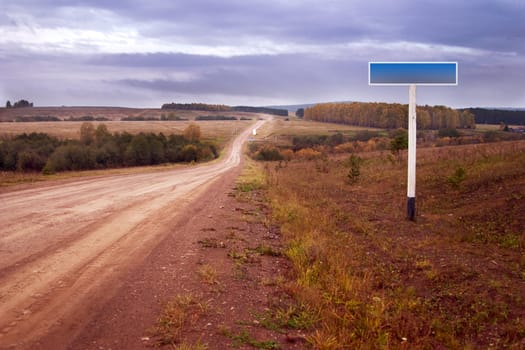 Autumn landscape: cart-dirt road and an empty road sign