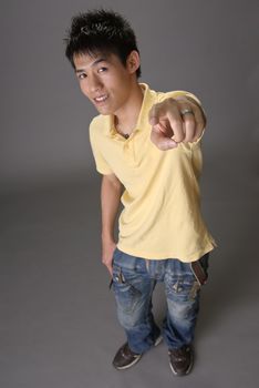 Asian young guy point at you over studio gray background.